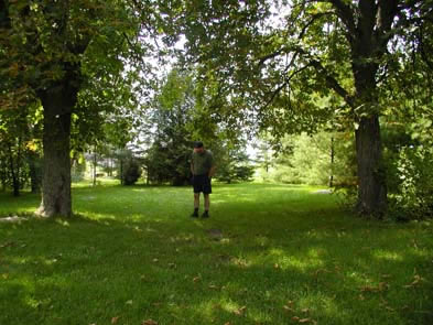 [ Donnelly Homestead As It Appears Today, Owner Robert Salts stands where the Donnelly home was once located before it was burned in 1880.  The trees in the photograph are two of the five horse-chestnut trees that William planted in memory of his five murdered family members. Thanks to Robert Salts, present-day owner of the Donnelly Homestead, who allowed this photograph to be taken. Copyright Great Unsolved Canadian Mysteries Project, Jennifer Pettit,   ]